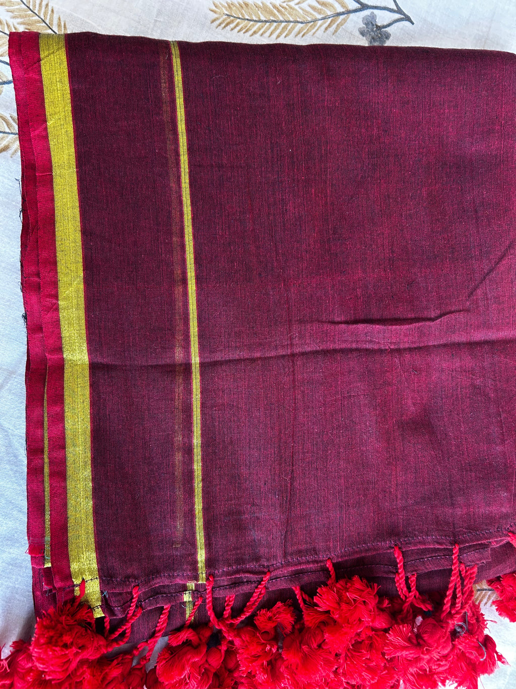 Maroon fabric with red tassels and gold stripes on a white background