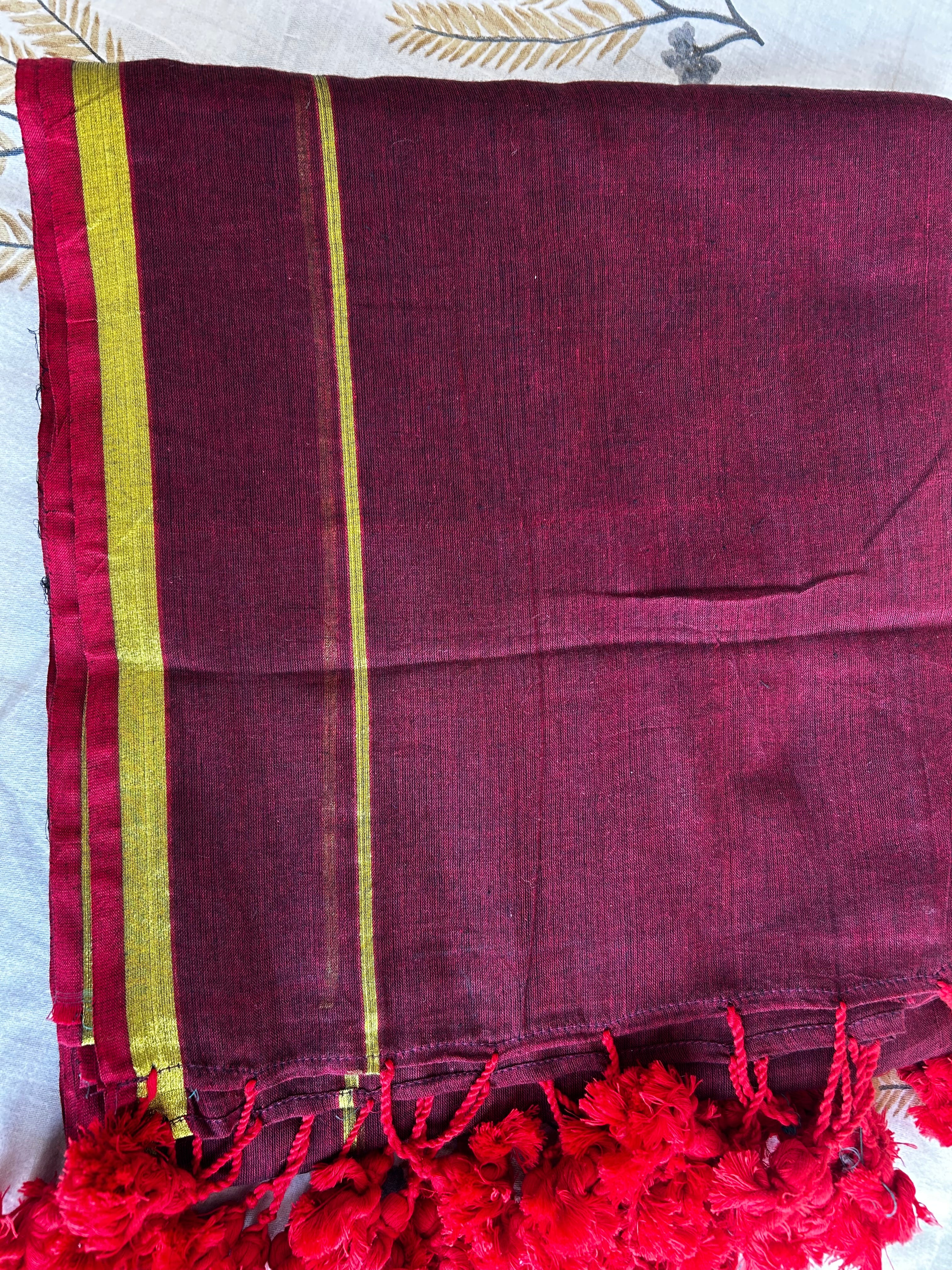 Maroon fabric with red tassels and gold stripes on a white background